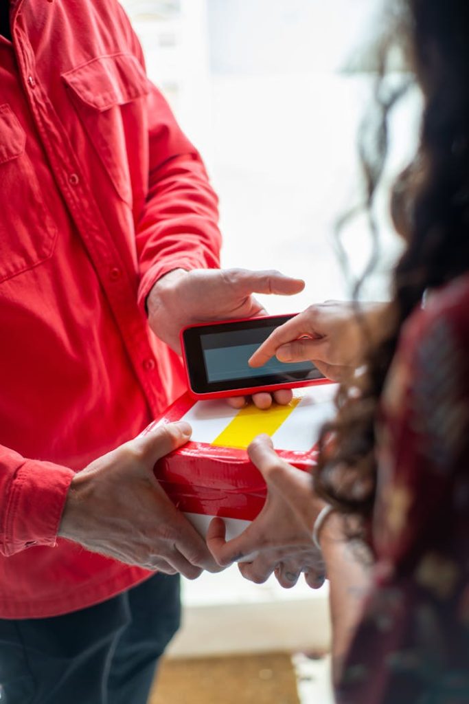 woman-picking-package-from-a-delivery-man-6721915 A delivery person in red hands a package to a customer for electronic signature, highlighting e-commerce convenience.